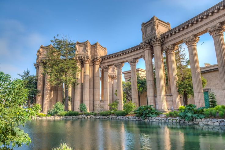 an old building with columns next to a body of water in front of trees and bushes