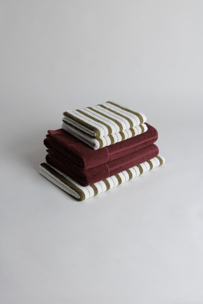 five folded towels stacked on top of each other in various colors and patterns, with one folded up to the side