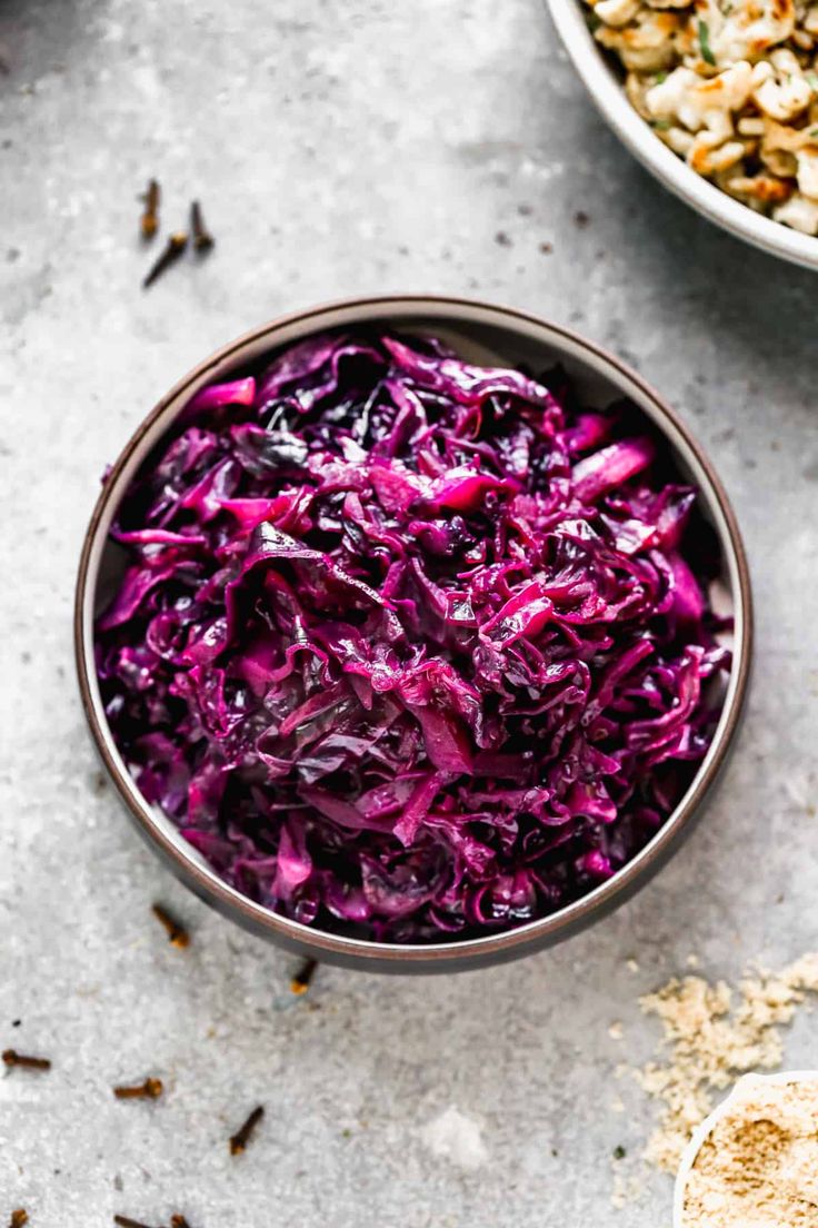 a bowl filled with red cabbage next to another bowl full of nuts and other food