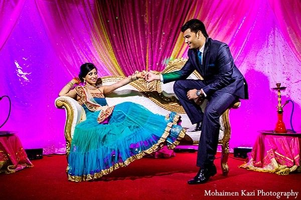 a man and woman sitting on top of a couch in front of a purple backdrop