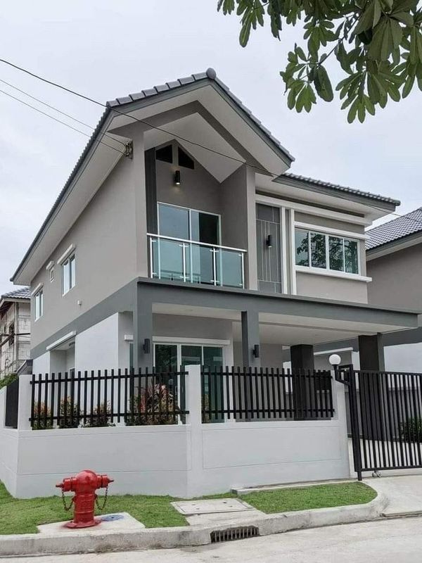 a red fire hydrant sitting in front of a gray two story house with a black fence