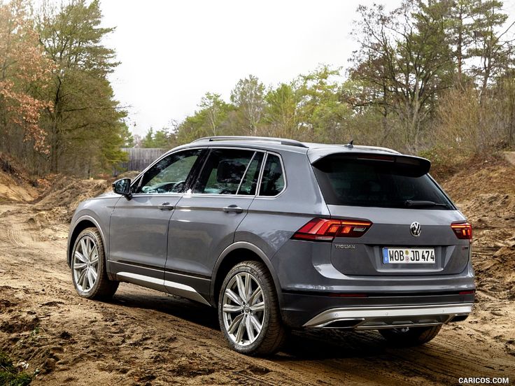 the rear end of a grey volkswagen tigua driving on a dirt road with trees in the background