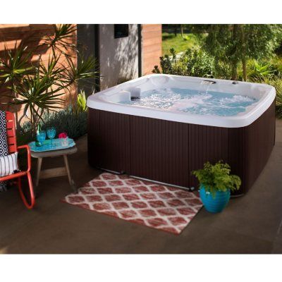 a hot tub sitting on top of a patio next to a chair and potted plant