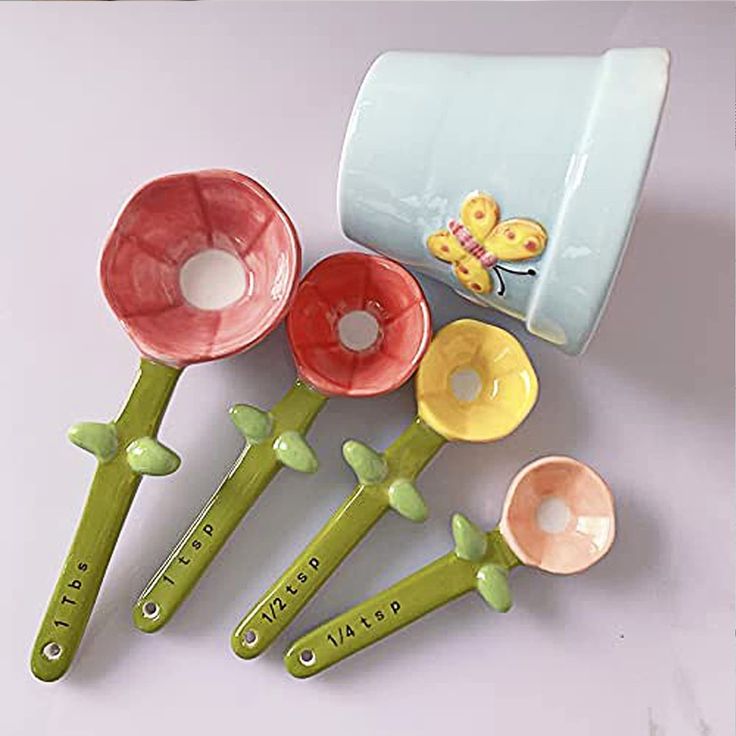 five ceramic spoons with flowers on them sitting next to each other in front of a cup