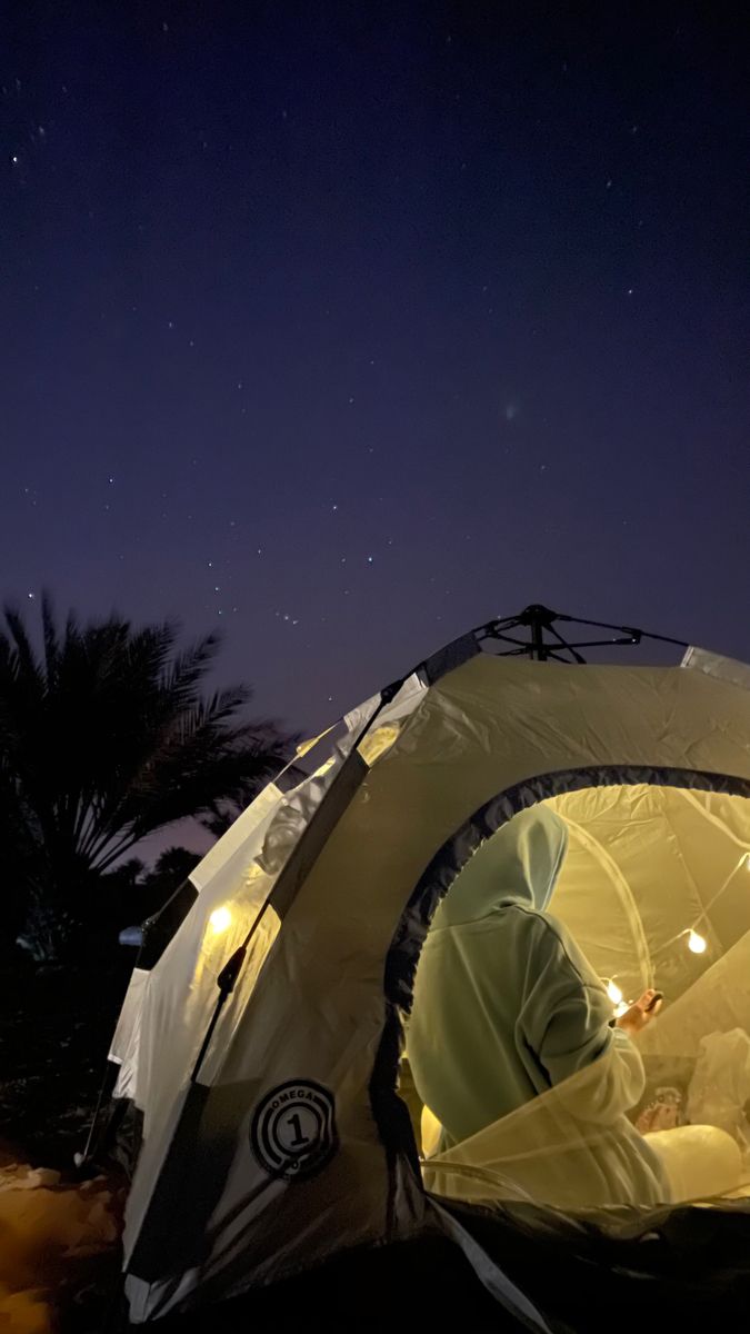 a man sitting inside of a tent under a night sky