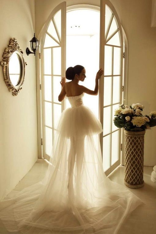 a woman standing in front of a doorway wearing a white dress and holding her hand up