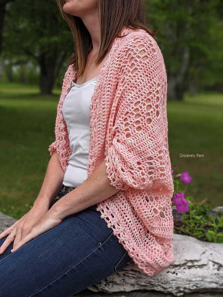 a woman sitting on a rock wearing a pink crocheted cardigan and jeans