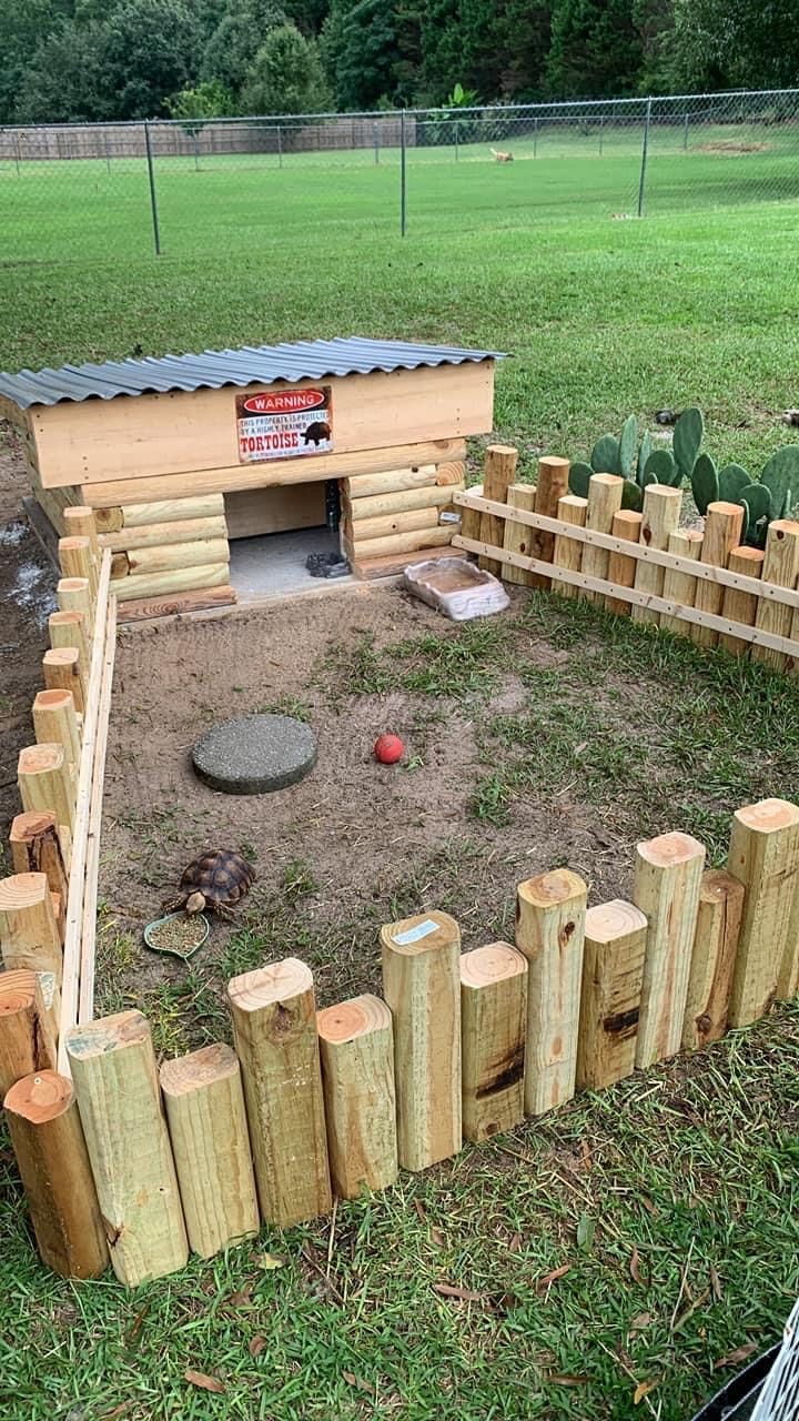 a dog house built into the side of a fenced in area with logs around it