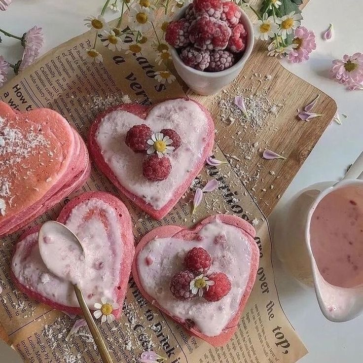 four heart shaped pastries with raspberries and flowers in them on top of a newspaper