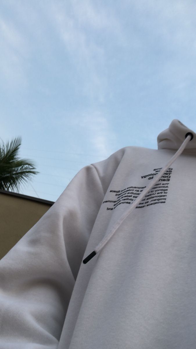 a person wearing a white hoodie with black writing on the side and palm trees in the background