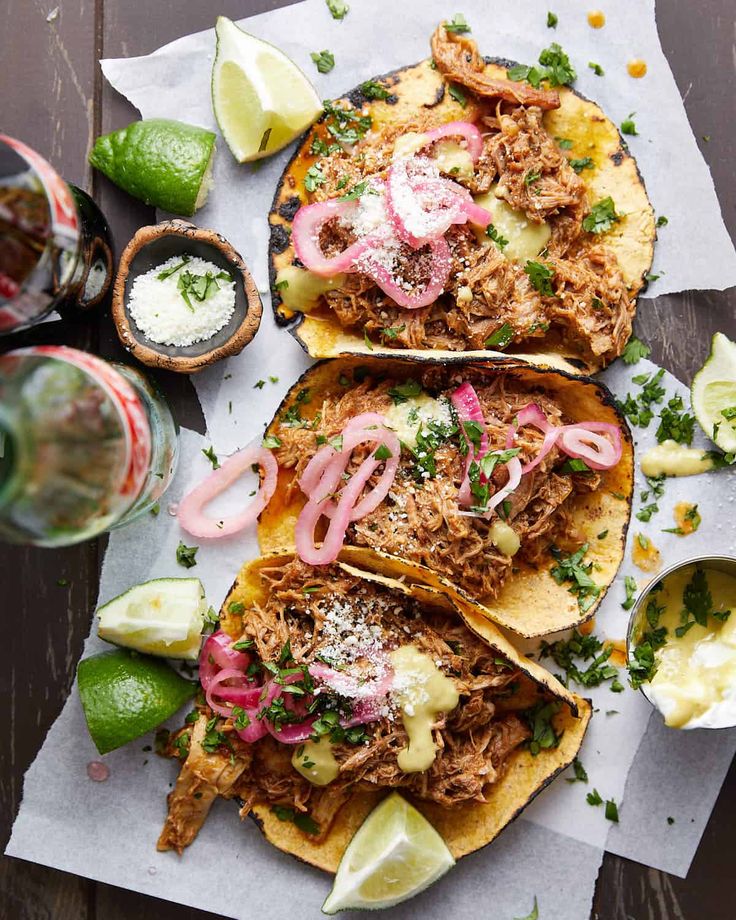 three tacos with meat, onions and sour cream on paper next to some limes