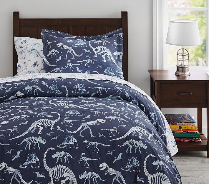 a bed with blue and white dinosaur comforters in a room next to a window