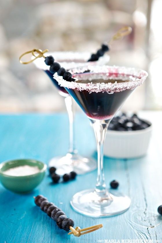 two glasses filled with blueberry martinis sitting on top of a table