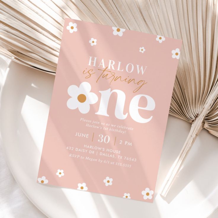 a pink and gold birthday party card with daisies on the front sitting on a plate