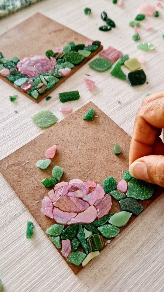 someone is making mosaics with pink flowers and green leaves on brown paper next to them