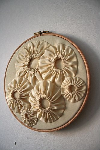 a white wall hanging with some flowers on it's side and an embroidered piece in the middle