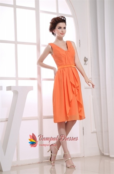 a woman in an orange dress standing next to a white wall and window with her hands on her hips