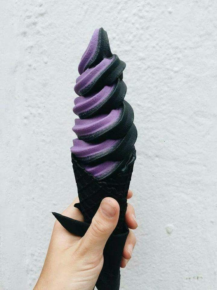 a hand holding an ice cream cone with purple and black icing