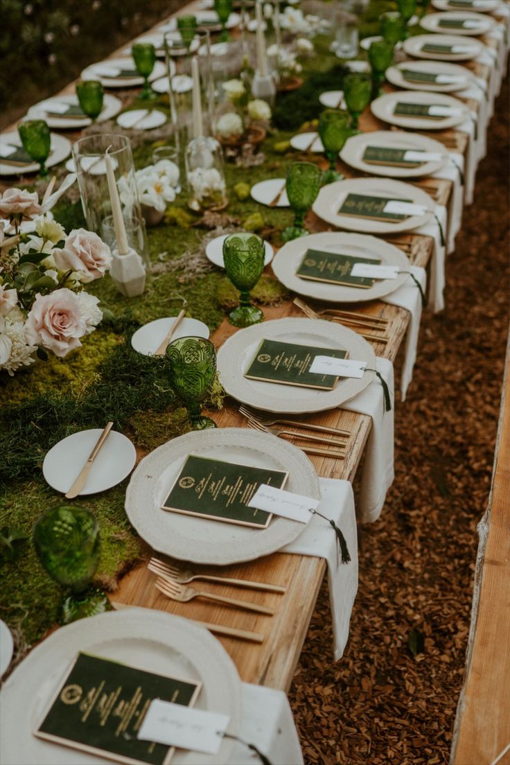 a long table is set with white plates and place settings for an outdoor dinner party