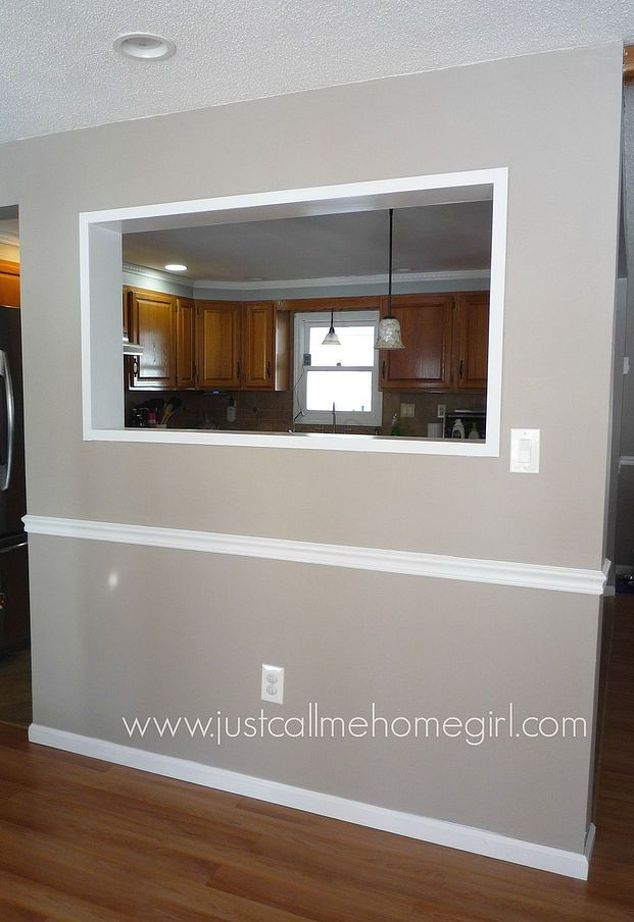 an empty living room and kitchen with wood flooring in the foreground, large mirror on the wall