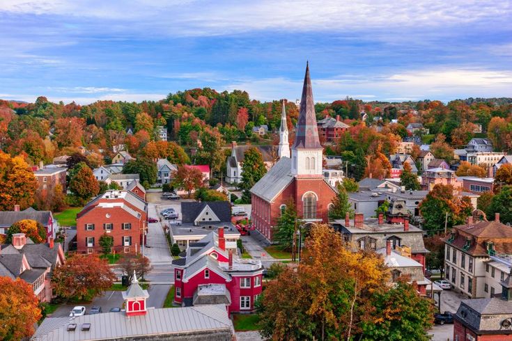 an aerial view of a small town surrounded by autumn trees and colorful foliage, with a church steeple in the center