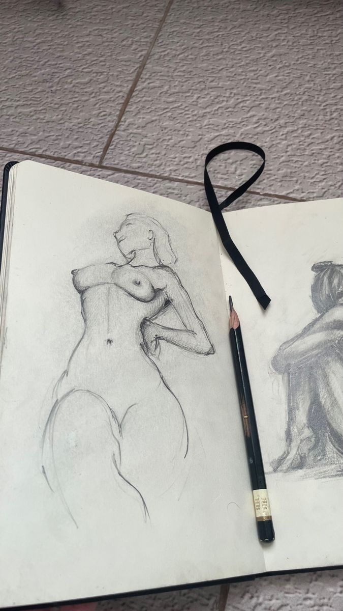 a pencil drawing of a nude woman next to a book with a black ribbon on it