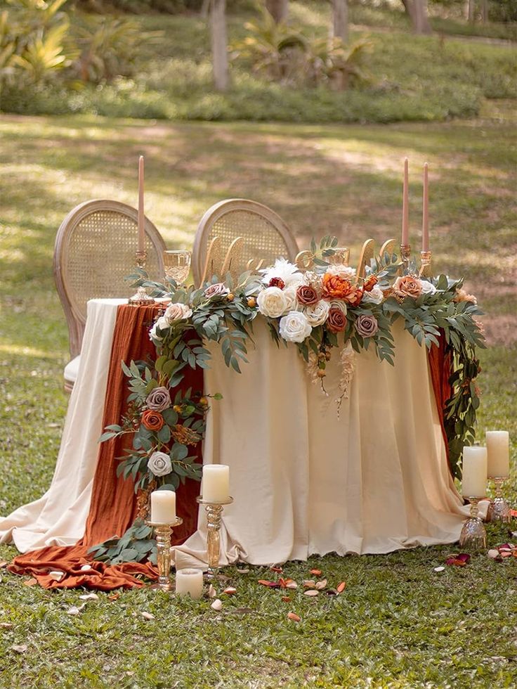 a table with candles and flowers on it in the middle of some grass, surrounded by chairs