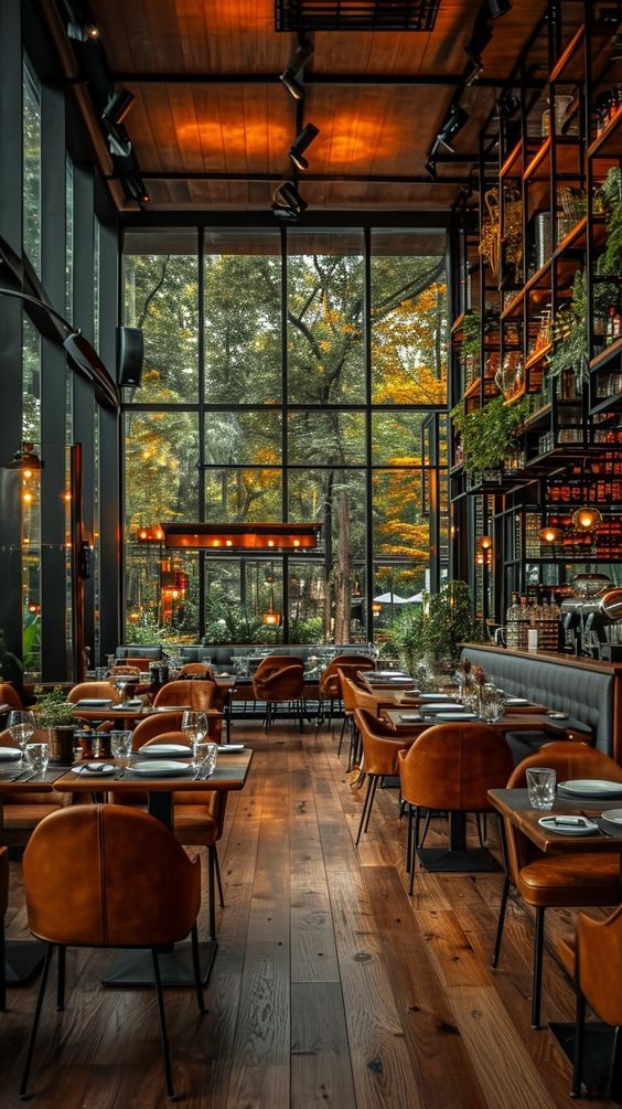 an empty restaurant with wooden tables and brown chairs, large windows, and lots of greenery