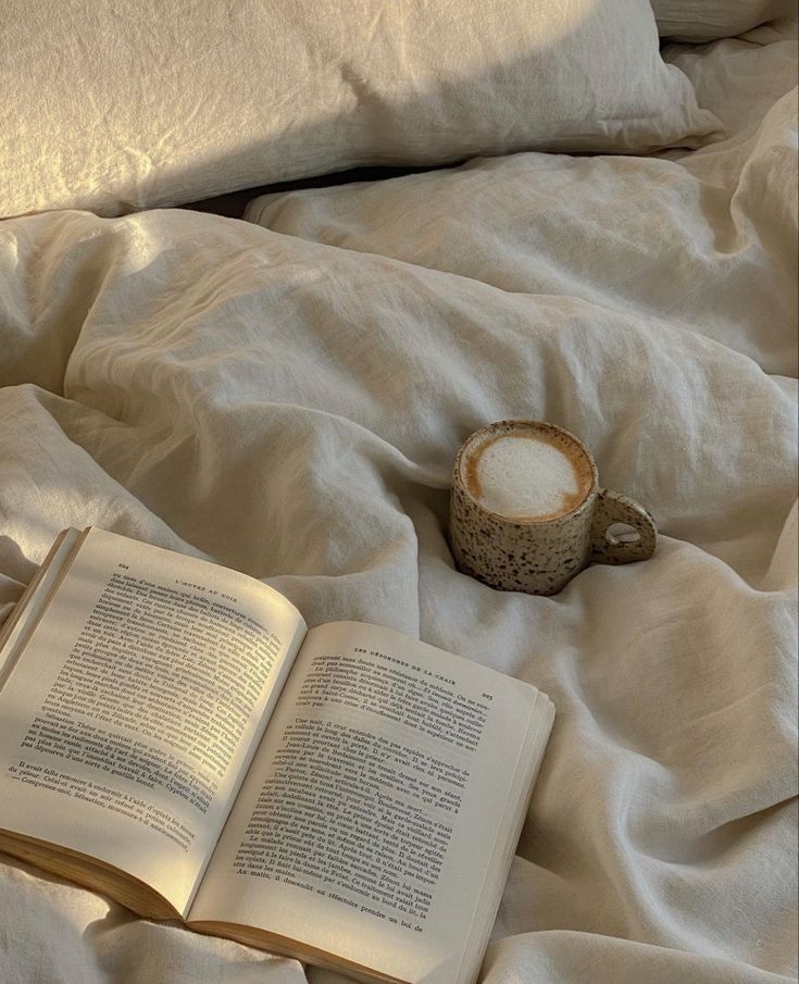 an open book sitting on top of a bed next to a cup and saucer