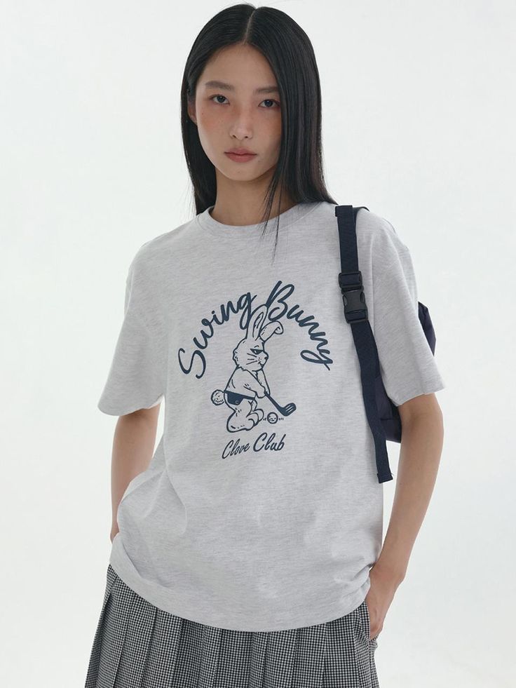 a young woman standing in front of a white background wearing a gray tshirt