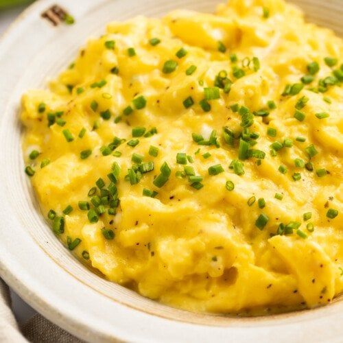 a white bowl filled with mashed potatoes and green onions on top of a table