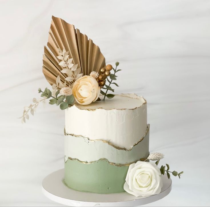 a white and green wedding cake with flowers on the top is decorated with gold leaves