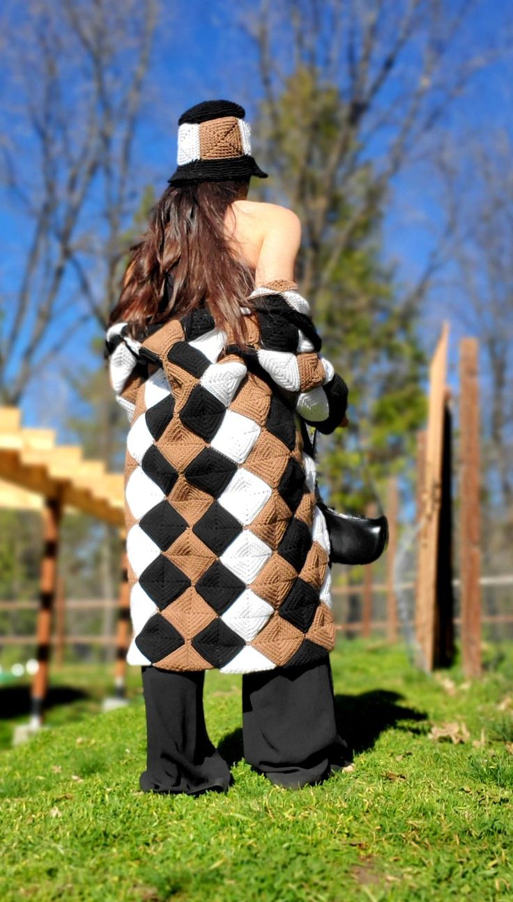 a woman standing in the grass wearing a black and white argyle sweater with her back turned to the camera