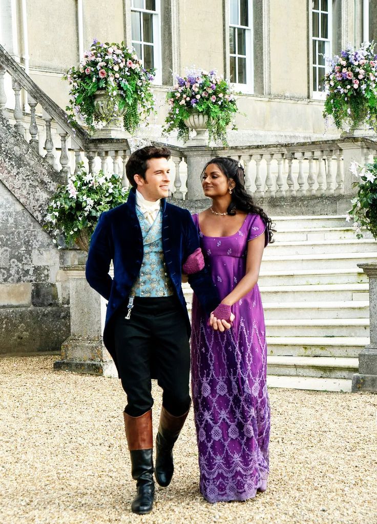 a man and woman dressed in period clothing walking down the street next to some stairs