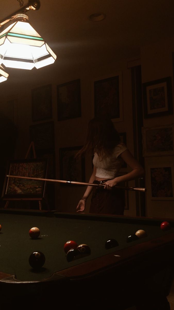 a woman standing in front of a pool table next to a light hanging from the ceiling