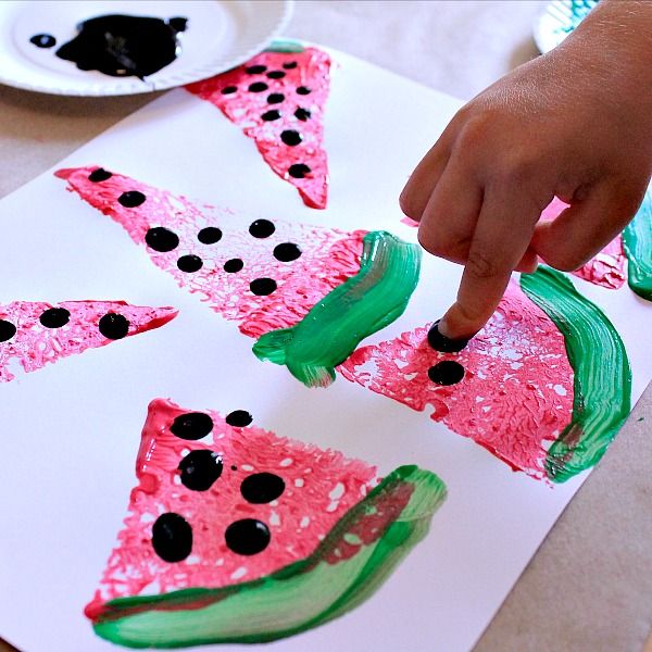 a child is painting watermelon slices on paper with black dots and green tips