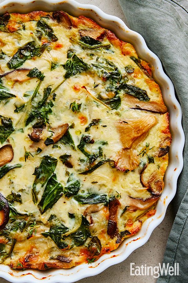 a quiche with spinach, mushrooms and cheese in a pie pan on a table