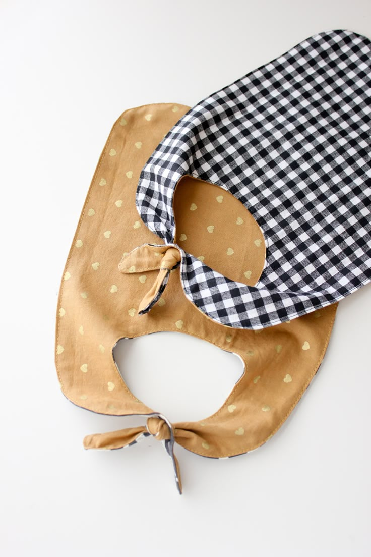 two baby bibs are laying next to each other on a white surface, one has a black and white checkered bandana