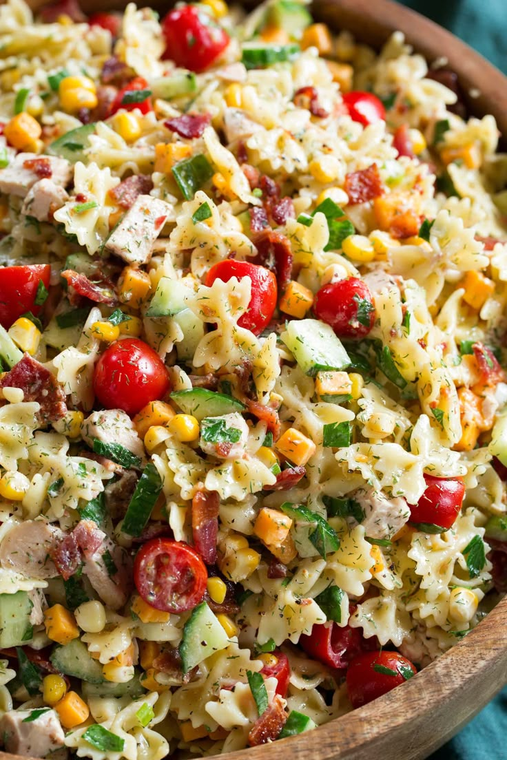 a wooden bowl filled with pasta salad on top of a blue table cloth next to a fork