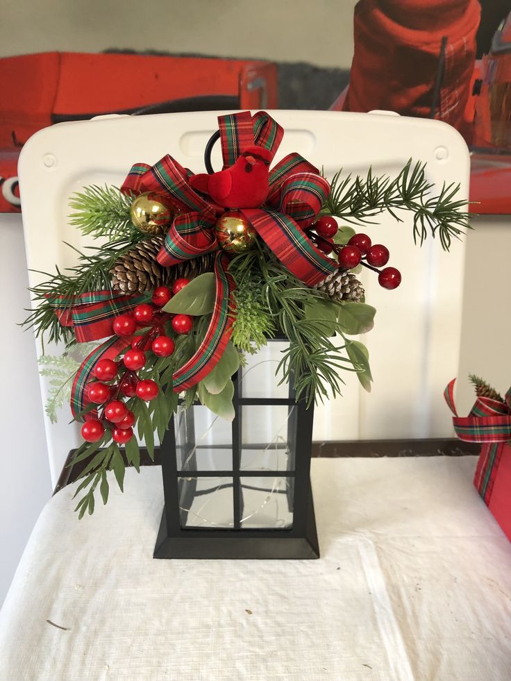 a christmas decoration with pine cones, berries and evergreens in a lantern style holder