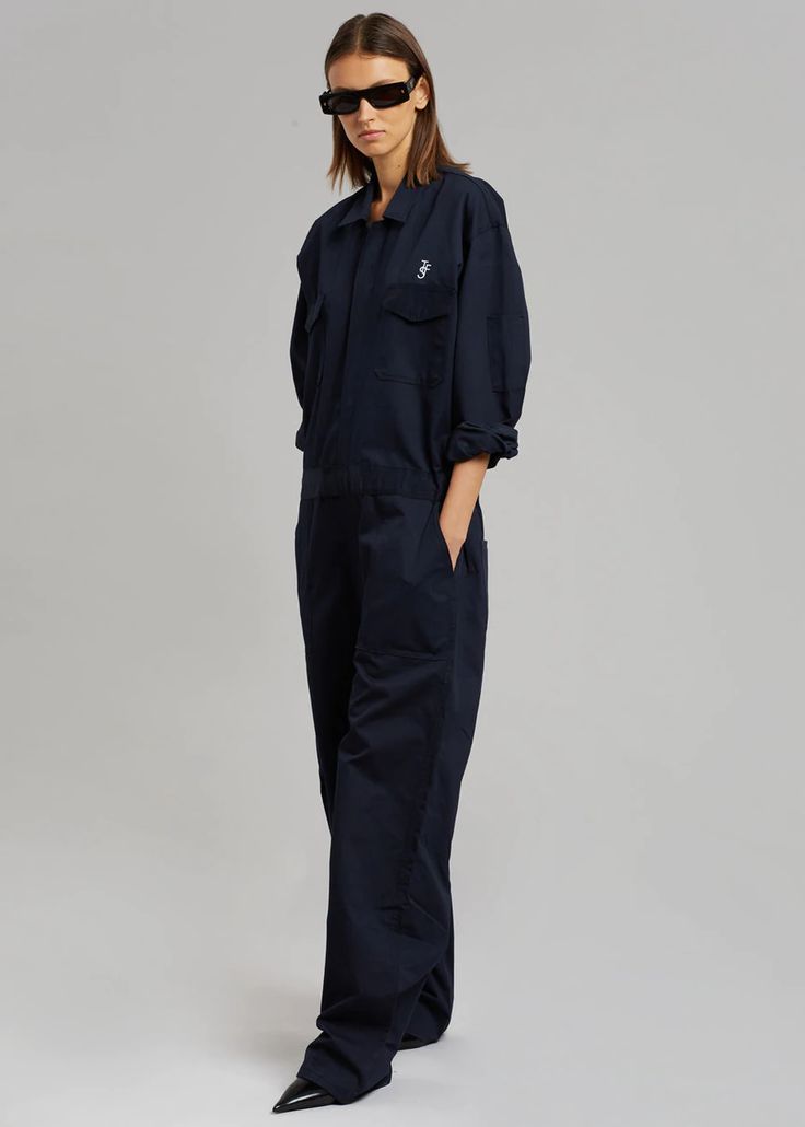 Color: Navy Unisex style Midweight twill fabric Oversized cargo jumpsuit Straight leg Pointed collar  The Frankie Shop logo embroidered on the front and back Elastic tabs at side waist Front flap chest pockets Slant hip pockets Zip and velcro front closure Unlined 65% Polyester 35% Cotton Dry Clean  By The Frankie Shop Utility Cotton Cargo Jumpsuits And Rompers, Utility Cotton Jumpsuits And Rompers In Cargo Style, Utility Style Cotton Jumpsuits And Rompers With Cargo Details, Utility Cotton Jumpsuit With Multiple Pockets, Utility Cotton Jumpsuits And Rompers With Multiple Pockets, Utility Denim Jumpsuit With Pockets For Work, Workwear Denim Overall Jumpsuit With Patch Pockets, Utility Cotton Jumpsuits And Rompers With Patch Pockets, Utility Jumpsuits And Rompers With Patch Pockets