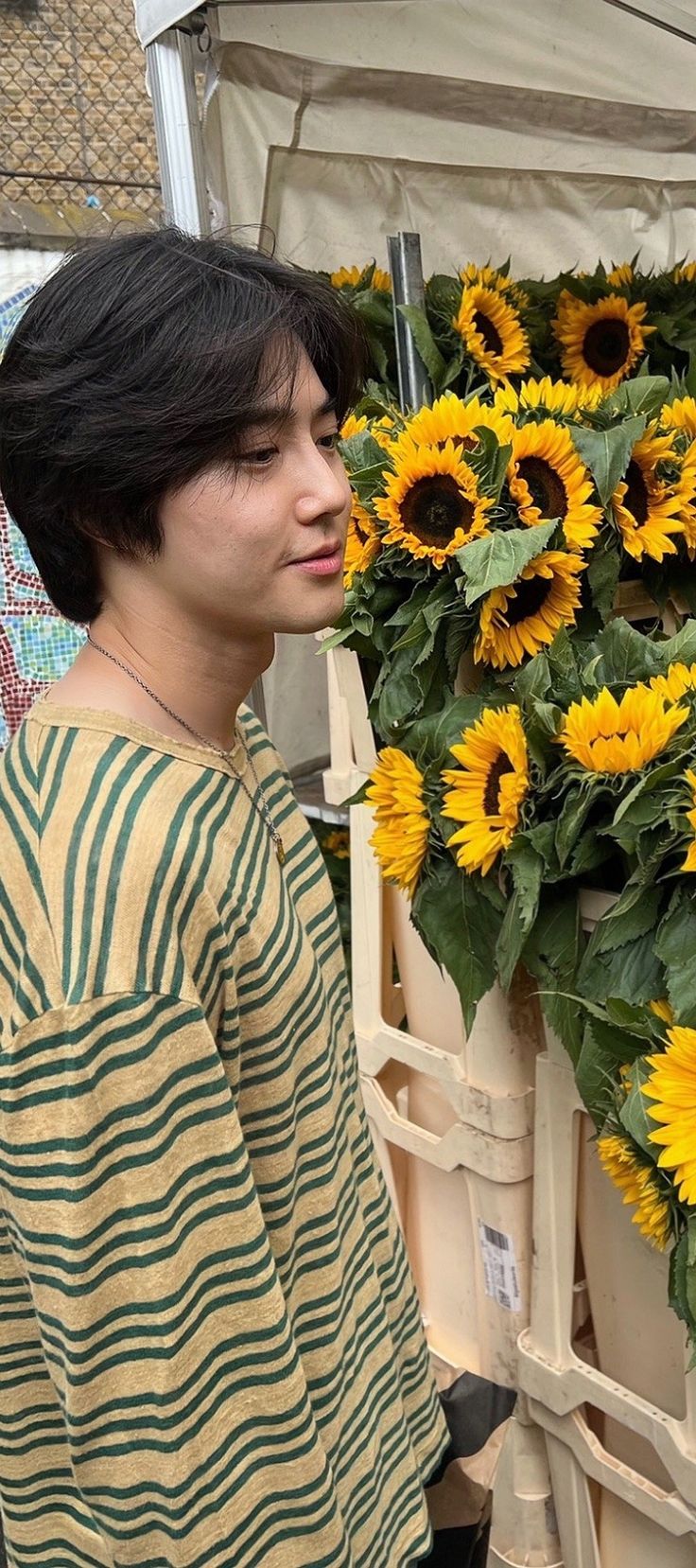 a young man standing next to a bunch of sunflowers in a flower shop