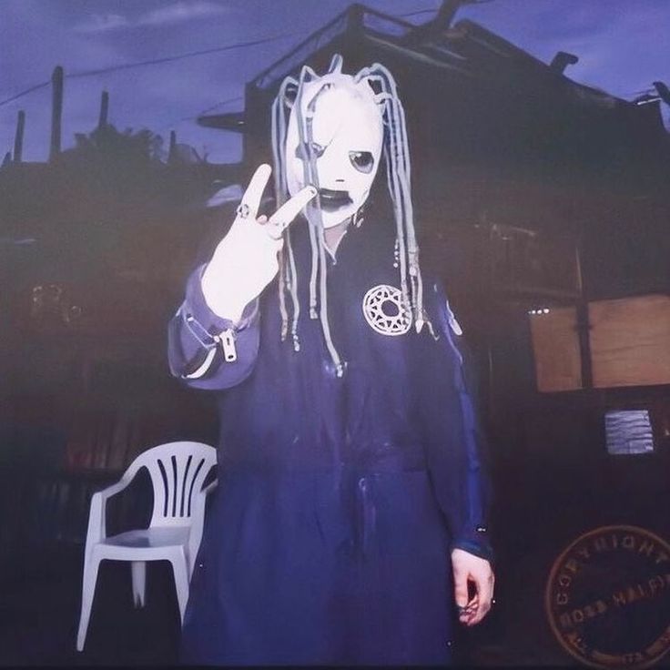 a man with dreadlocks standing in front of a house wearing an alien mask