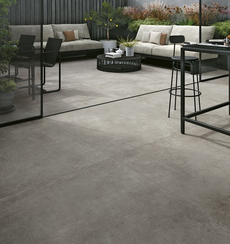 an outdoor living area with couches, tables and stools on concrete flooring