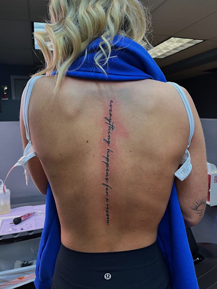 the back of a woman's upper body, showing her tattoos and writing on it