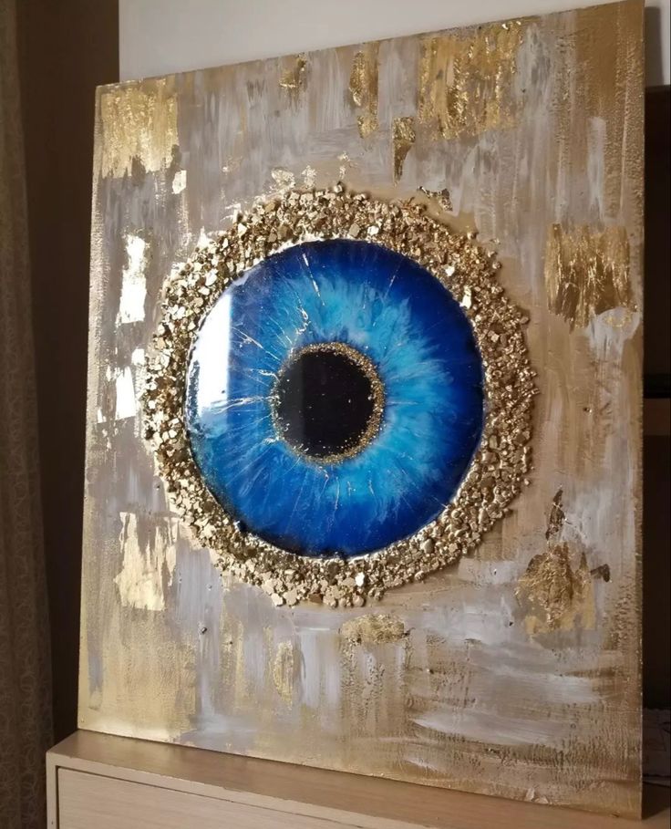 an eyeball painted on a piece of wood with gold and blue eyeshade