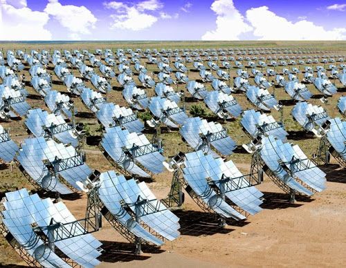 rows of solar panels in the middle of a field with blue sky and clouds behind them