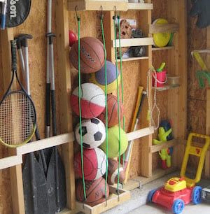 there are many sports items in the storage room on this shelf, including balls and rackets