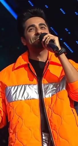 a man in an orange jacket singing into a microphone