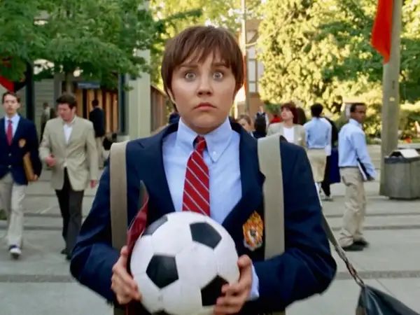 a man in a suit holding a soccer ball on the street with people walking behind him